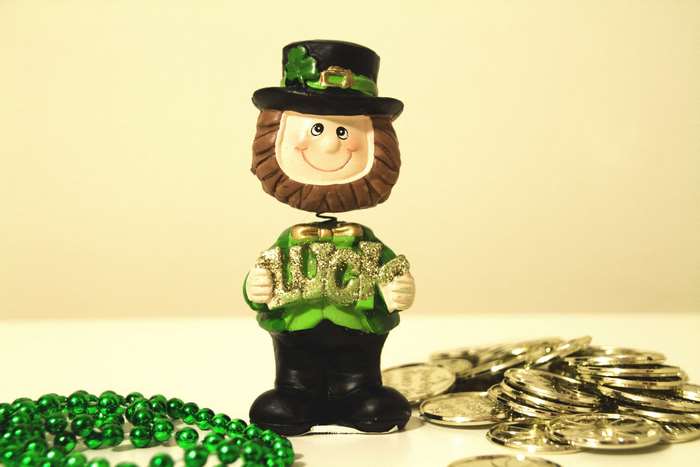 Leprechaun holding "LUCK" with gold coins and green beads