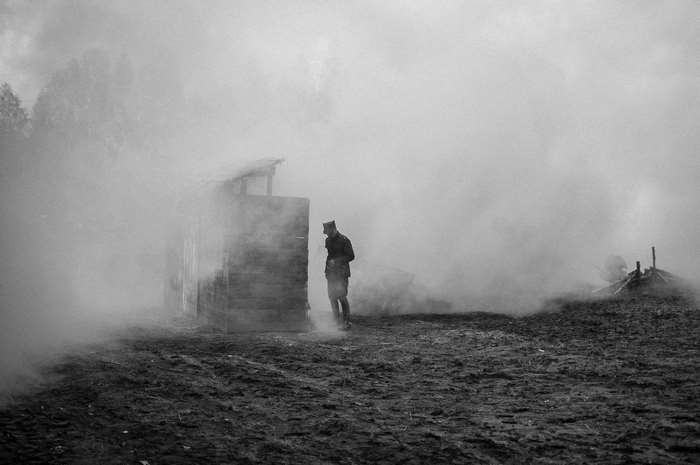 Soldier in smoke near a wooden structure during World War II