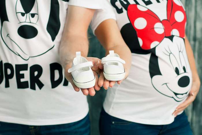 Couple holding baby shoes with Disney characters
