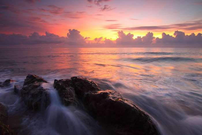 Ocean waves crashing on rocks at sunrise or sunset