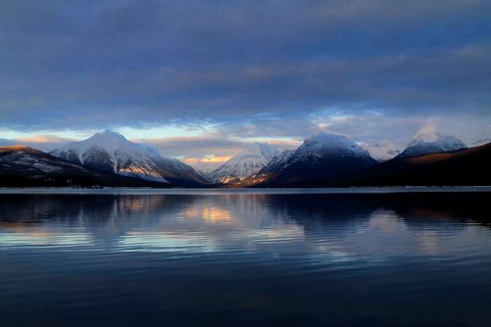 Snow-capped mountains reflected in a calm lake at dusk
