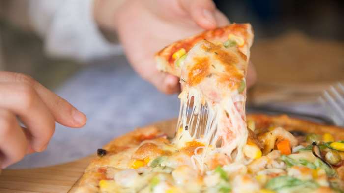 Close-up of a hand holding a slice of pizza with melted cheese
