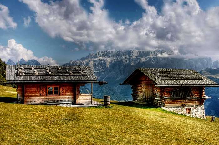 Two wooden cabins on a grassy hillside with mountains in the background