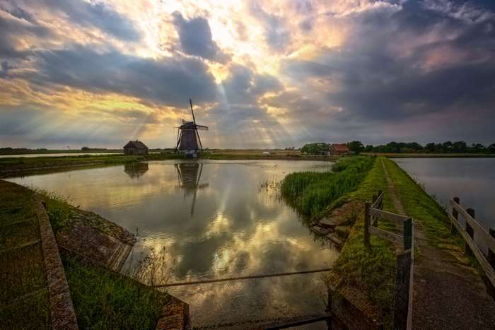 Windmill and pond in Netherlands with sun rays