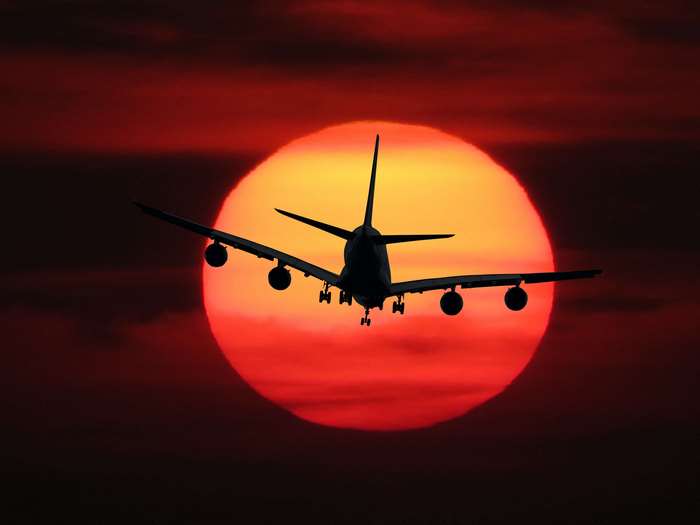 Airplane flying in front of a large sunset