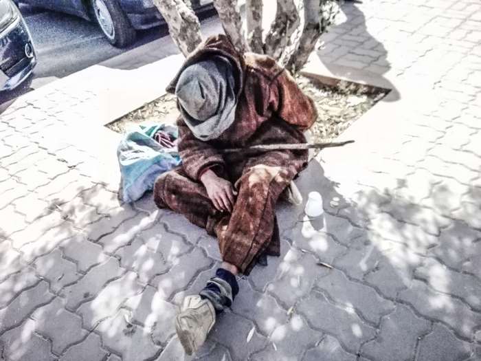 Poor man sitting on the street with a stick