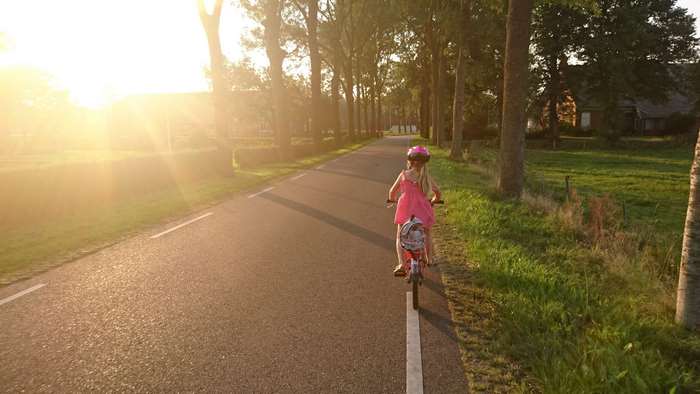 Girl in pink dress riding a bicycle on a sunny road
