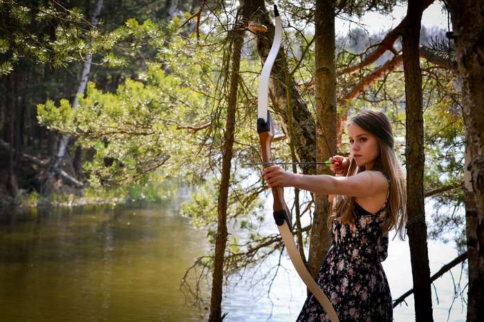 Young woman aiming a bow and arrow in a forest by the water