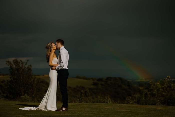 Bride and groom kissing with rainbow in dark sky