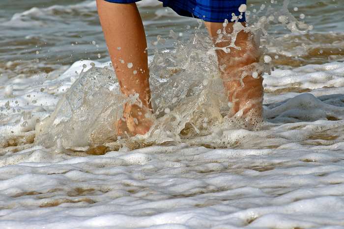 Feet splashing in ocean waves on a sandy beach