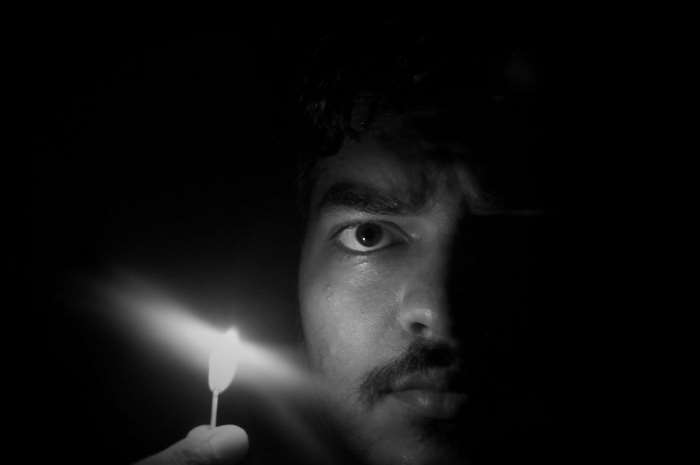 Man holding a lit matchstick in the dark