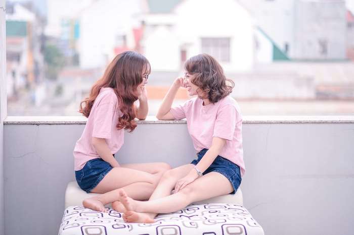 Two young women in pink t-shirts and denim shorts talking