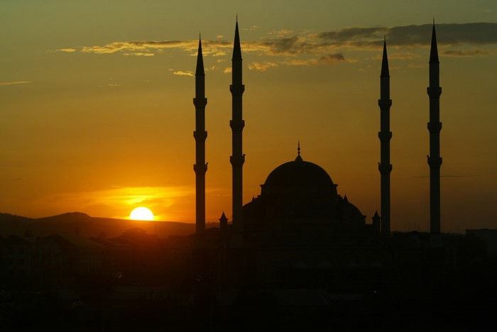 Mosque minarets and dome silhouetted against a sunset