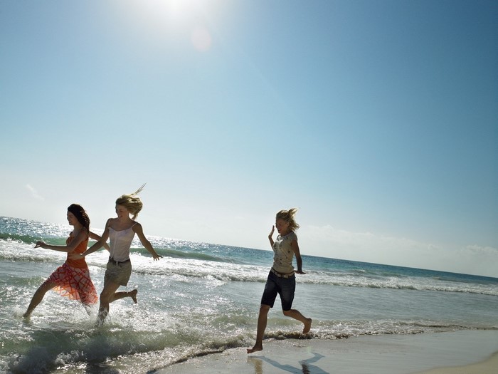 Three girls running on a beach by the sea