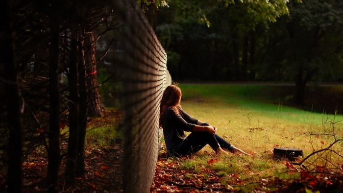 Girl sitting alone by a fence in a park
