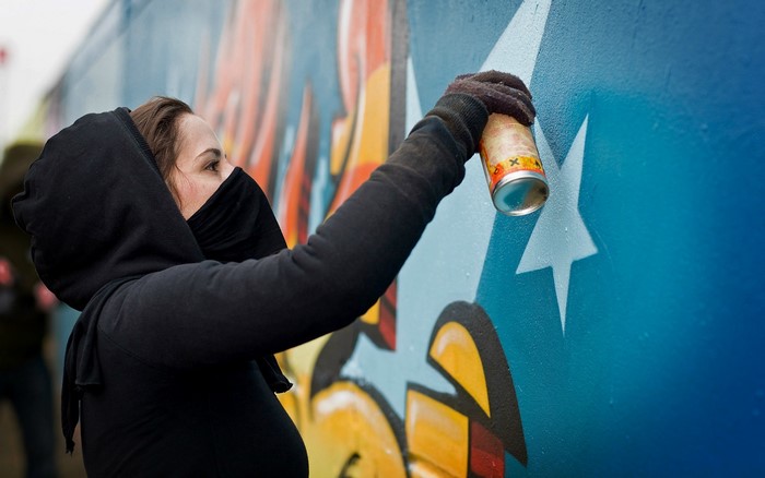 Girl in black hoodie spray painting a graffiti wall