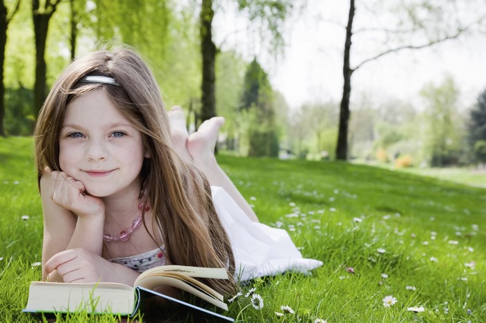 A young girl reading a book in a park