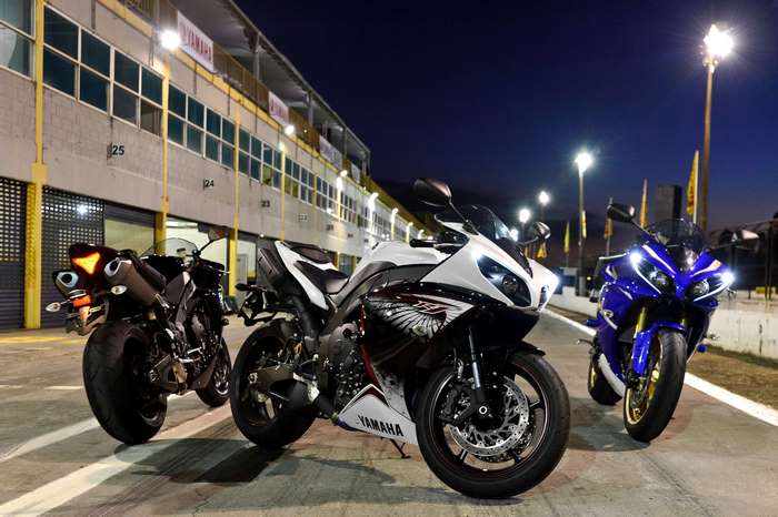 Three Yamaha R1 motorcycles parked at a race track at night