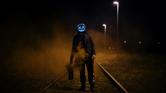 Man with glowing mask on railroad with smoke