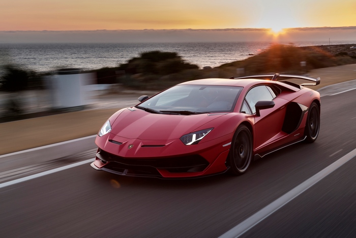 Red Lamborghini Aventador SVJ driving on a coastal road at sunset