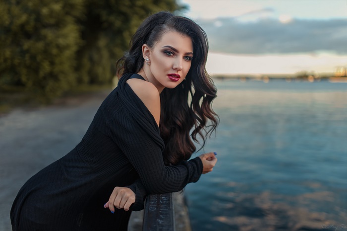 Woman with long dark hair and red lipstick by the water