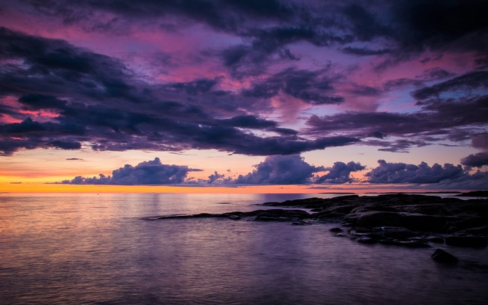 Purple clouds over the ocean at sunset with rocks