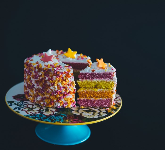 Layered rainbow cake with star sprinkles on a floral cake stand