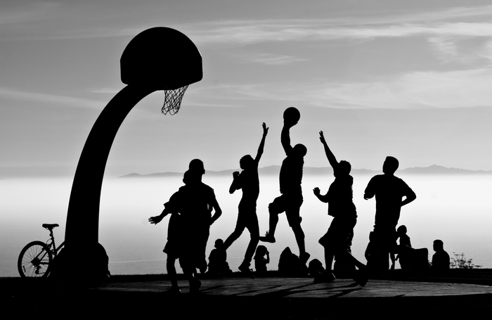 Silhouettes of people playing basketball at sunset
