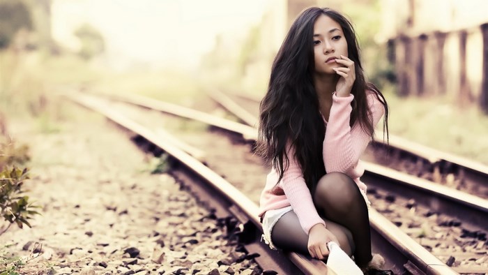 Young woman sitting on train tracks