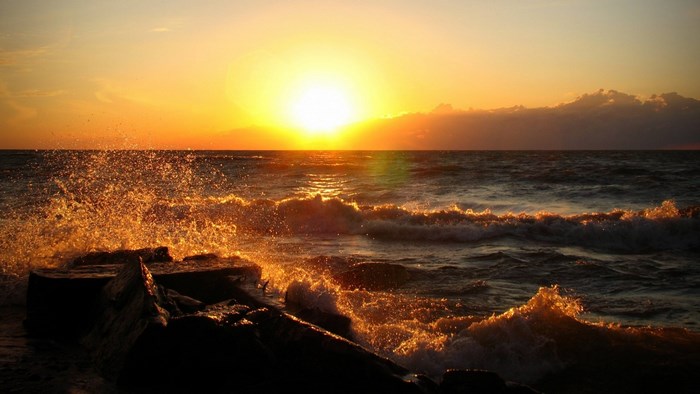 Sunset over the ocean with waves crashing on rocks