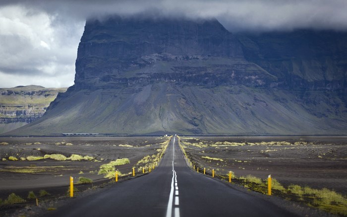 Road leading to a large mountain under cloudy sky