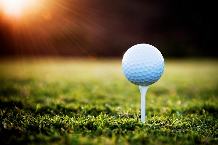 Golf ball on a tee in grass at sunset