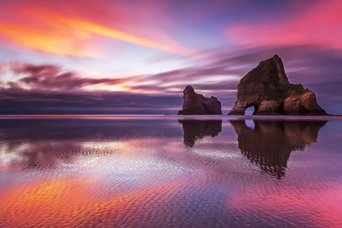 Sunset over ocean with rock formations and reflection
