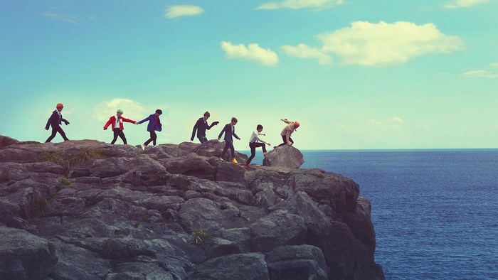 BTS members walking on a rocky cliff by the sea