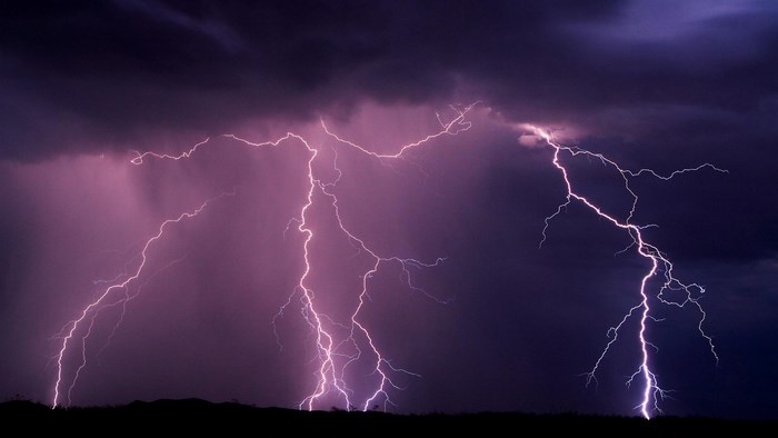 Lightning strikes during a thunderstorm over a dark landscape