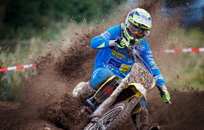 Motocross rider in blue and yellow gear kicking up dirt