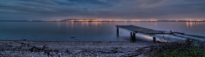 Wooden pier on a lake at dusk with city lights in the distance