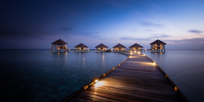 Overwater bungalows at sunset with illuminated walkway
