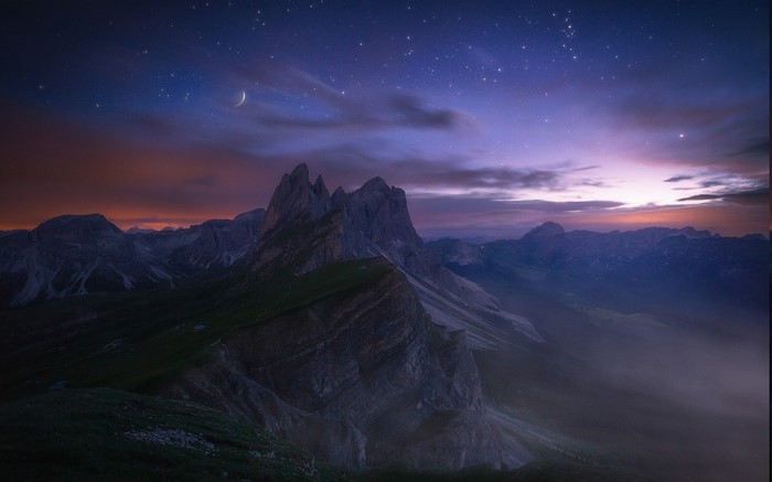 Mountain range under starry night sky with crescent moon