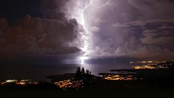 Lightning strikes over a bay with city lights at night