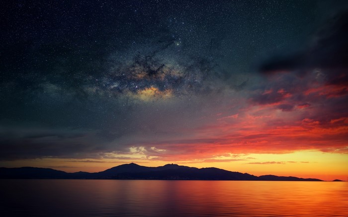 Milky Way over calm sea and mountains at sunset