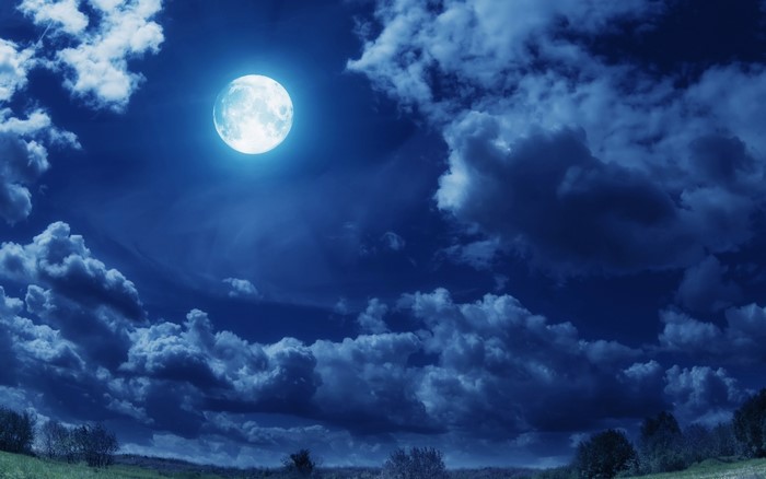 Full moon in a cloudy night sky over a landscape