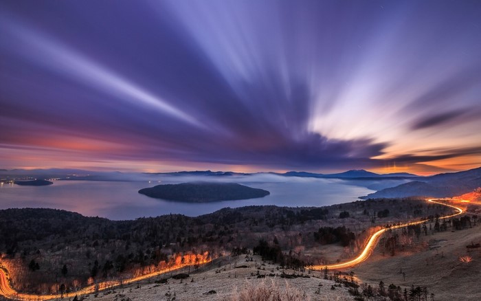 Long exposure sunset over a misty lake with light trails on a road