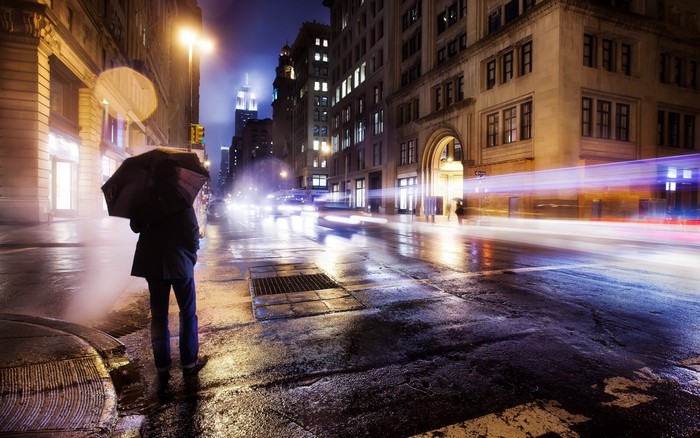 Person with umbrella on rainy city street at night