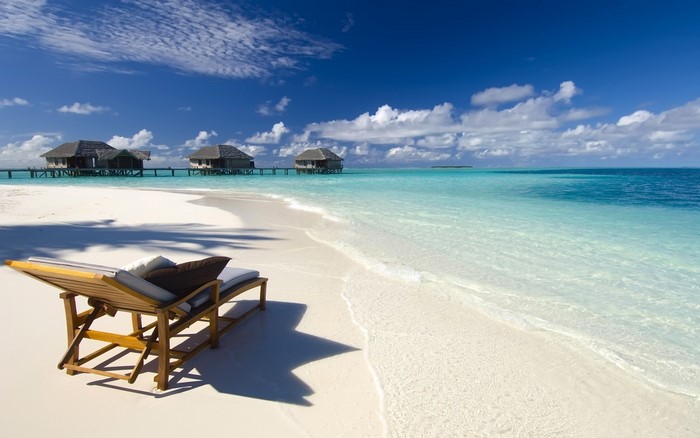 Maldives beach with overwater bungalows and lounge chair