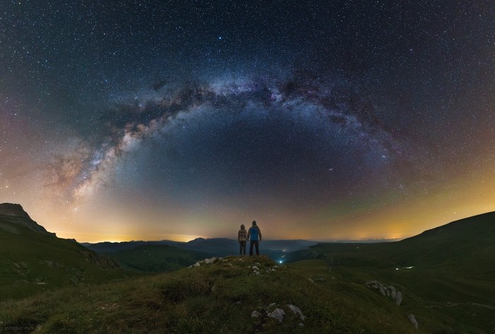 Two people looking at the Milky Way over mountains at night