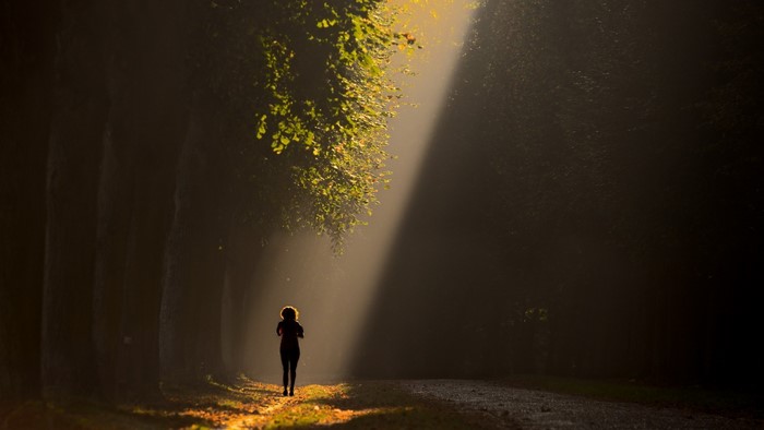 Woman running on a path in a forest with sunbeams