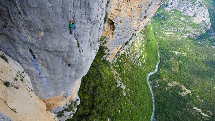Rock climber on a sheer cliff face overlooking a green valley