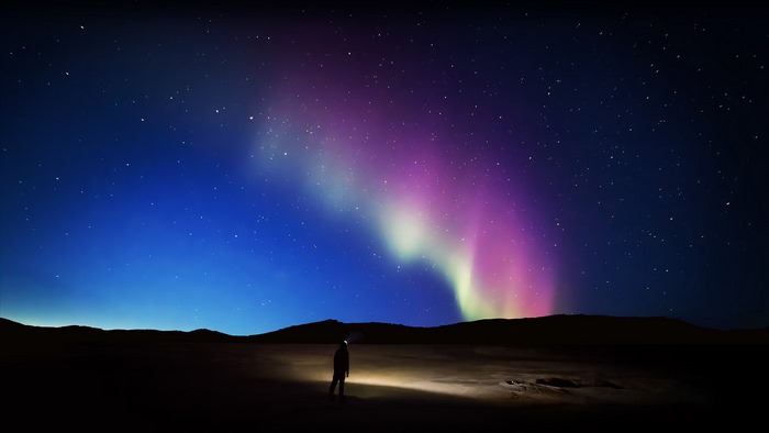 Person watching Aurora Borealis in a dark landscape