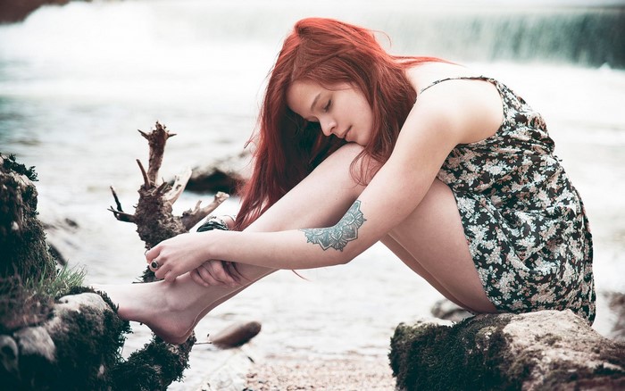 Redhead woman with tattoo sitting by water
